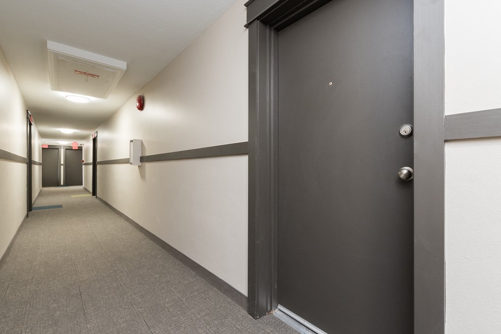 a black door in a long corridor with white walls and grey carpet