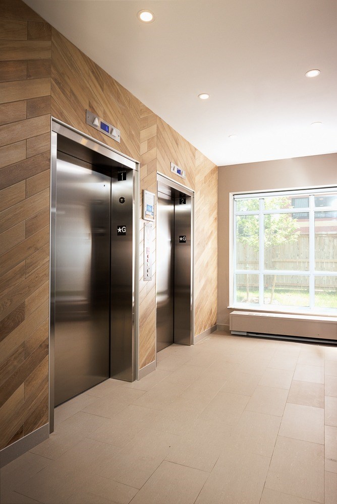 Two stainless steel elevators in a hallway with wood paneling on the walls.