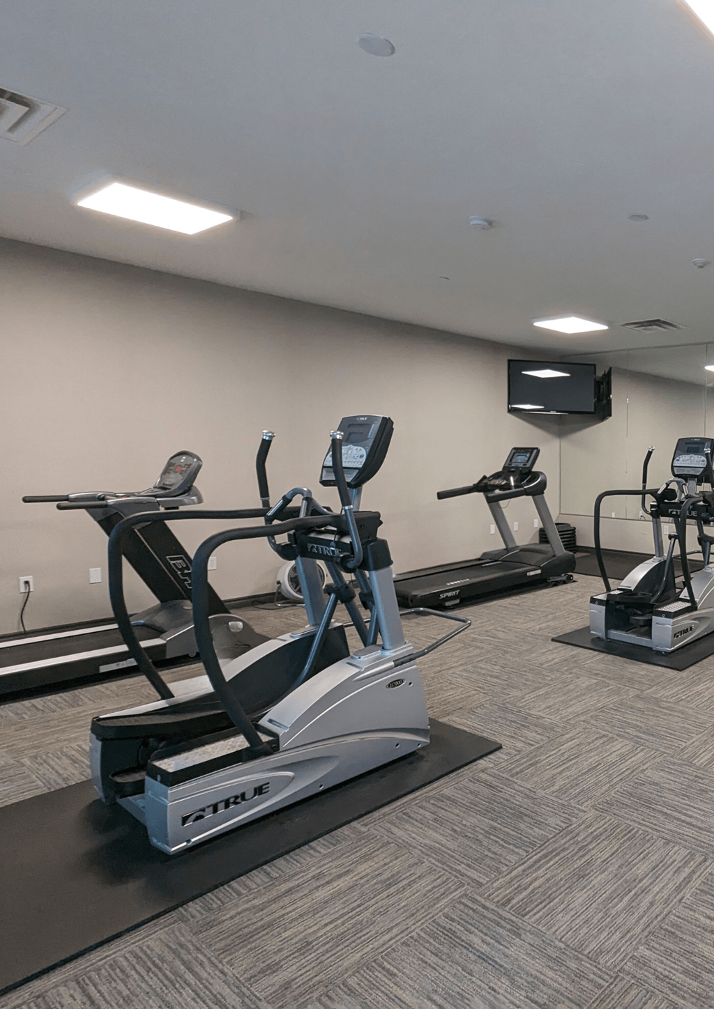 a gym with cardio equipment and a tv in a room