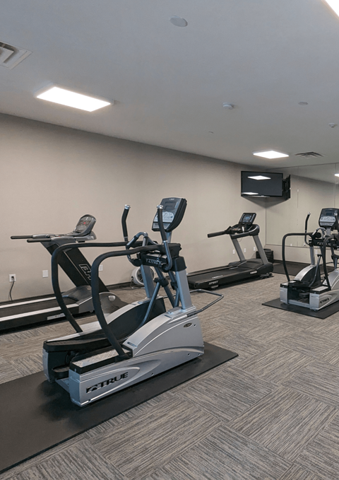 a gym with cardio equipment and a tv in a room