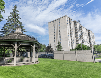 A gazebo sits in a grassy area in front of a tall building.