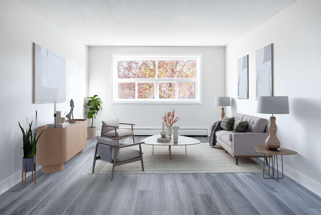 A living room with a grey sofa, a wooden table, and a large window with a view of trees.