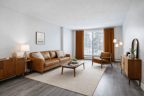 A living room with a brown leather sofa, a wooden coffee table, and a large window with orange curtains.