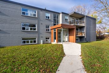 A modern two-story apartment building with a walkway leading to the front door.