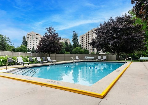 A swimming pool surrounded by trees and chairs.