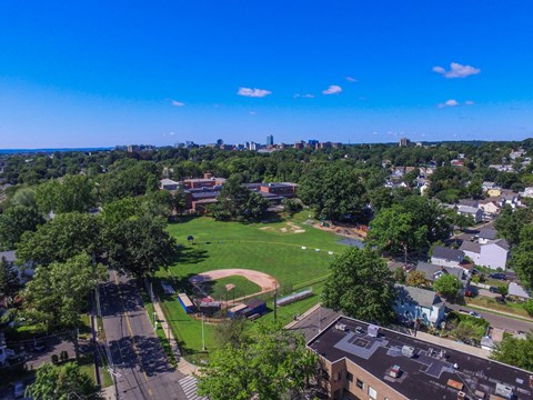 an aerial view of a baseball field with trees and a city skyline in the background