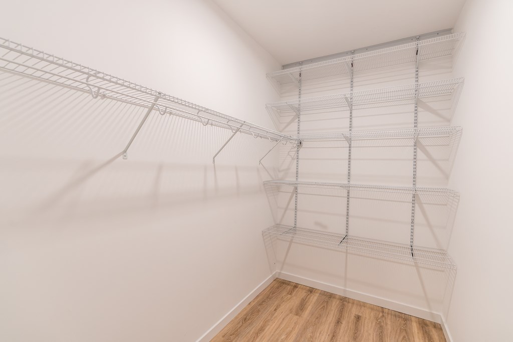 a walk in closet in a bedroom with white walls and hardwood floors