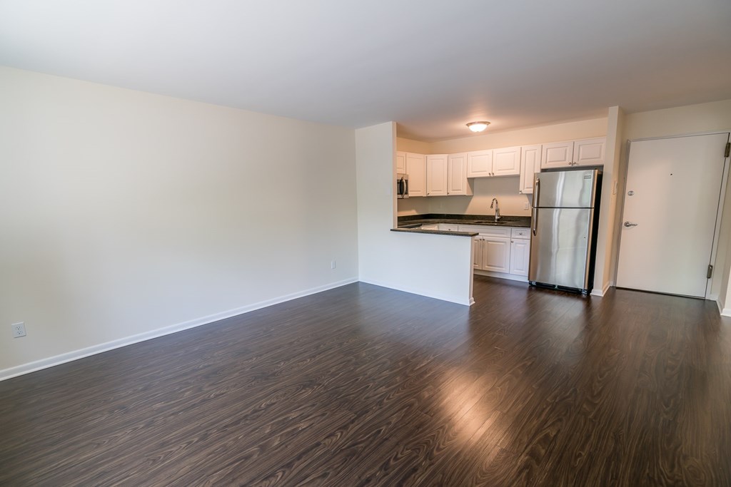 an empty living room and kitchen with wood flooring and a refrigerator