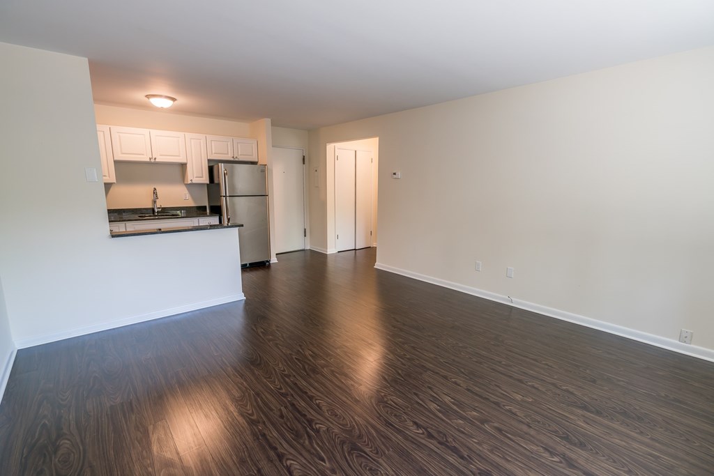 an empty living room with wood flooring and a kitchen