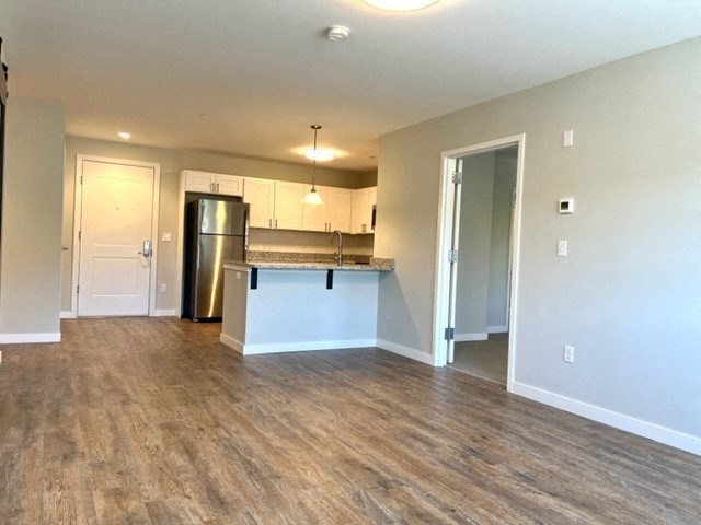an empty living room with a kitchen in the background