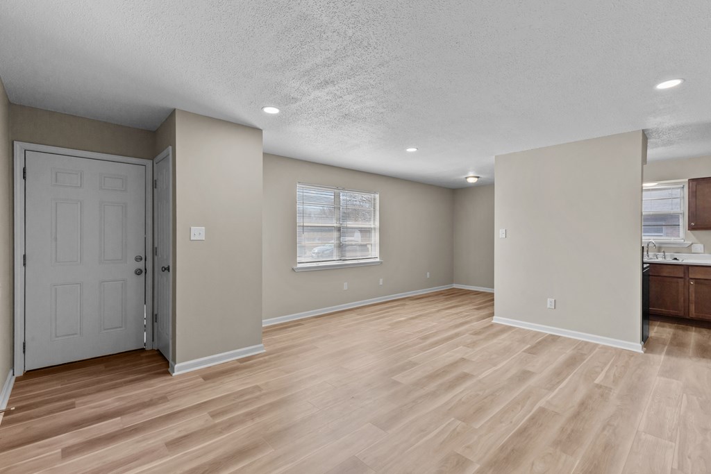 an empty living room with a door to a kitchen