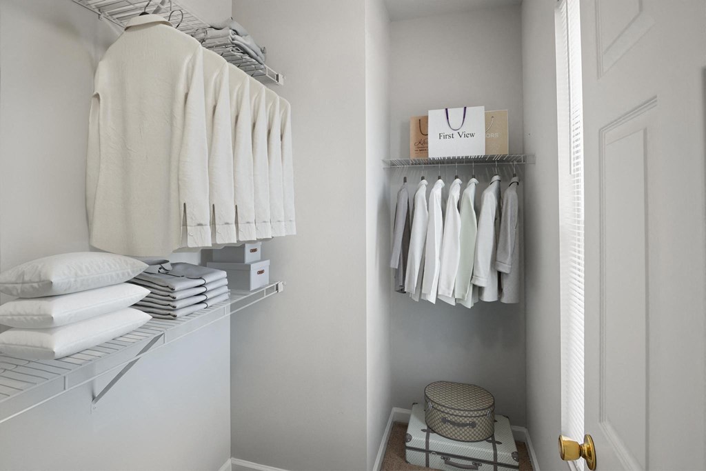 a small walk in closet with shelves and rails for clothing and a basket on the floor