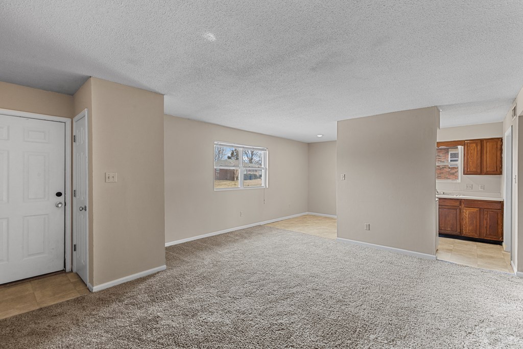 an empty living room with a door to a kitchen