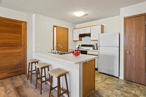 A kitchen with a white refrigerator, wooden bar stools, and a white countertop.