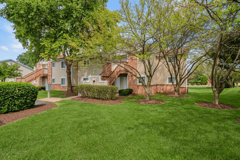 A grassy area in front of a building with a tree and bushes.