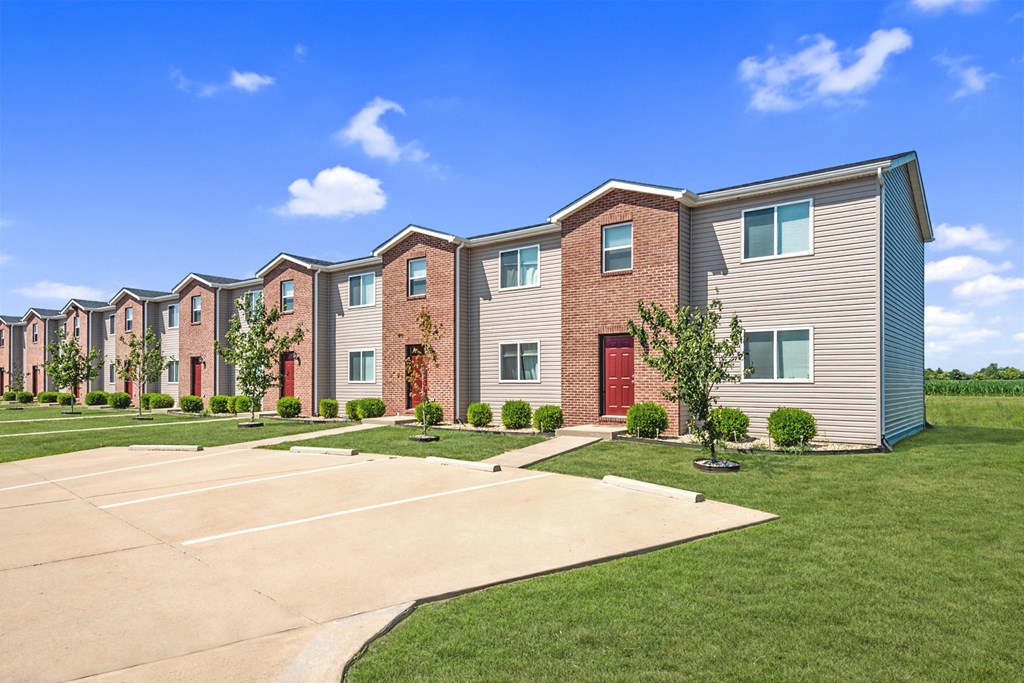an exterior view of a row of townhomes with green grass and a blue sky