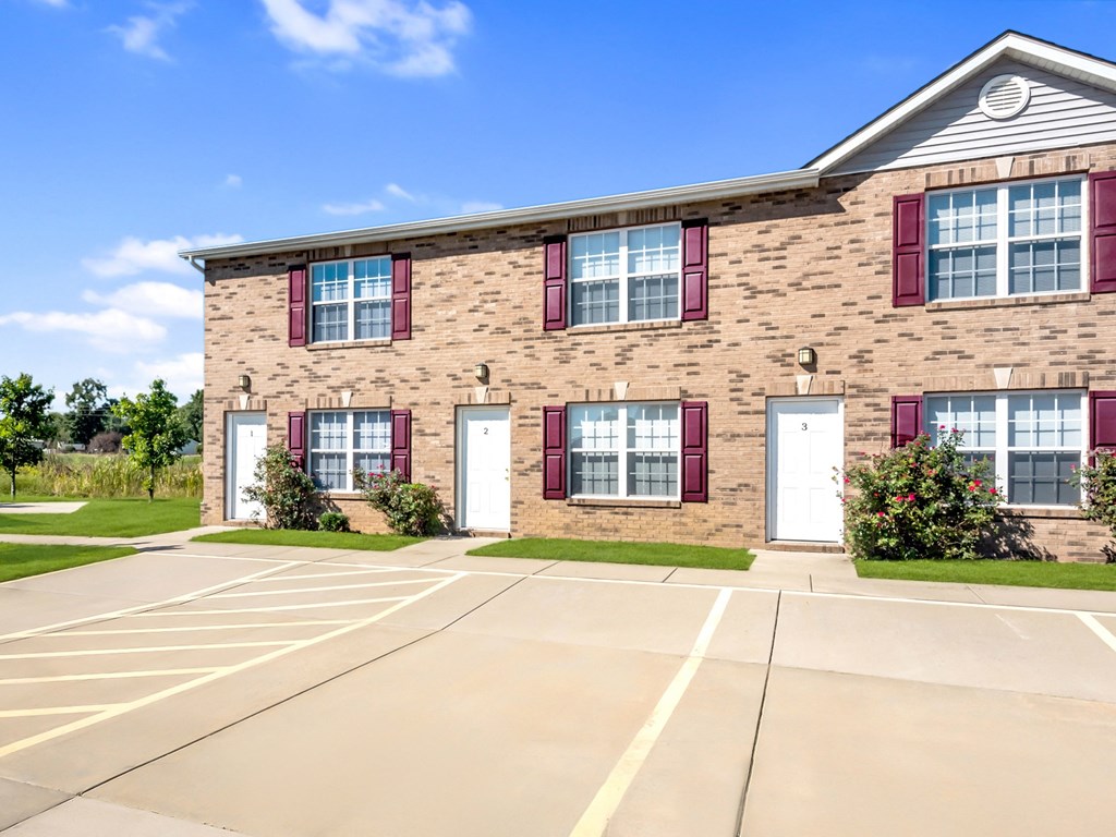 a brick building with red shuttered windows and a parking lot