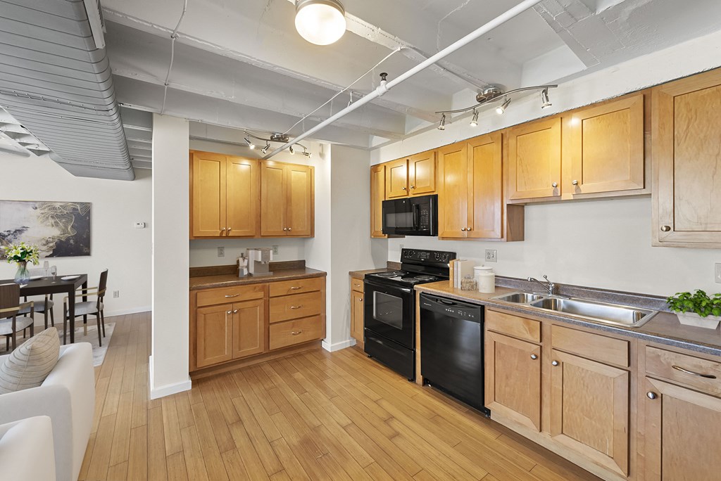 a kitchen with wooden cabinets and appliances and a living room with a table and chairs