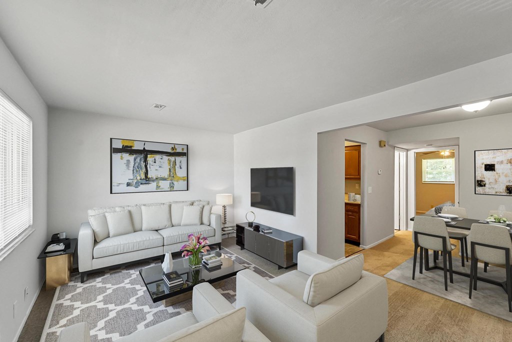 a living room with white couches and chairs and a tv on the wall
