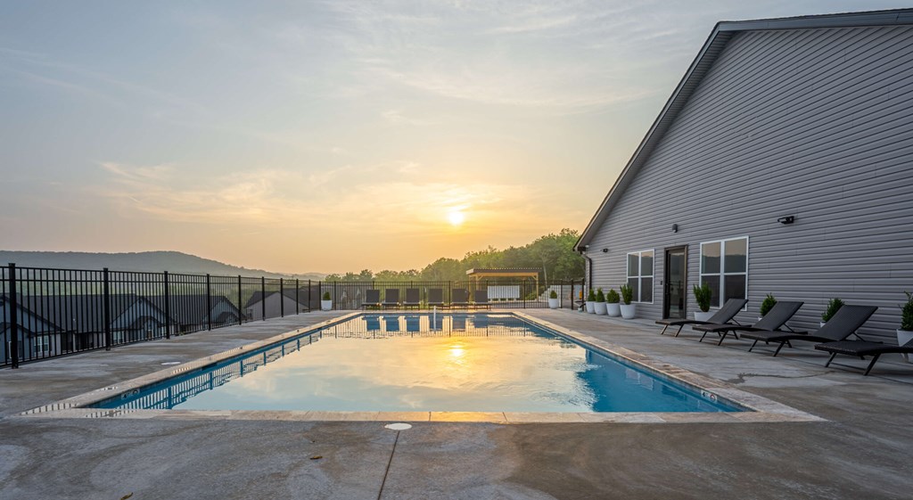 A sunset view of a pool with lounge chairs and a building in the background.