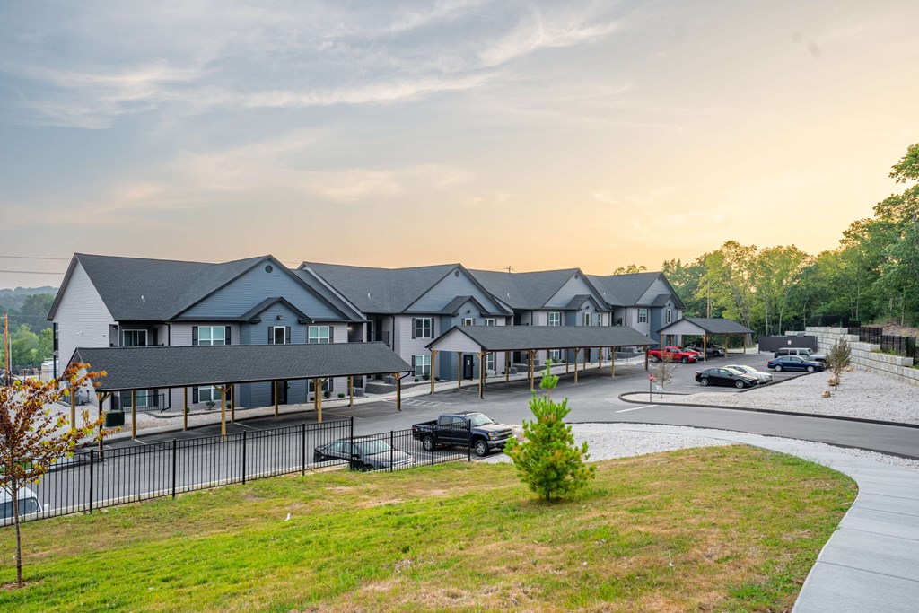 A large building with a grey roof and a parking lot in front.