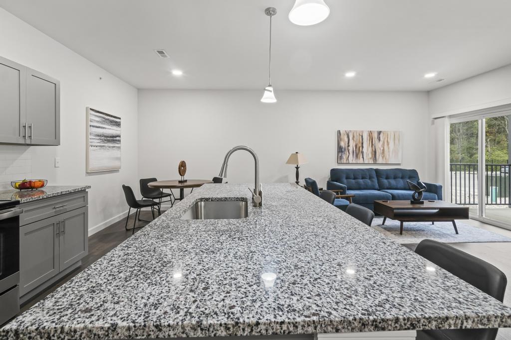 A kitchen with a granite countertop and a woman standing in front of it.