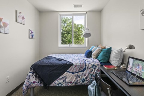 A bedroom with a bed, desk, and laptop.
