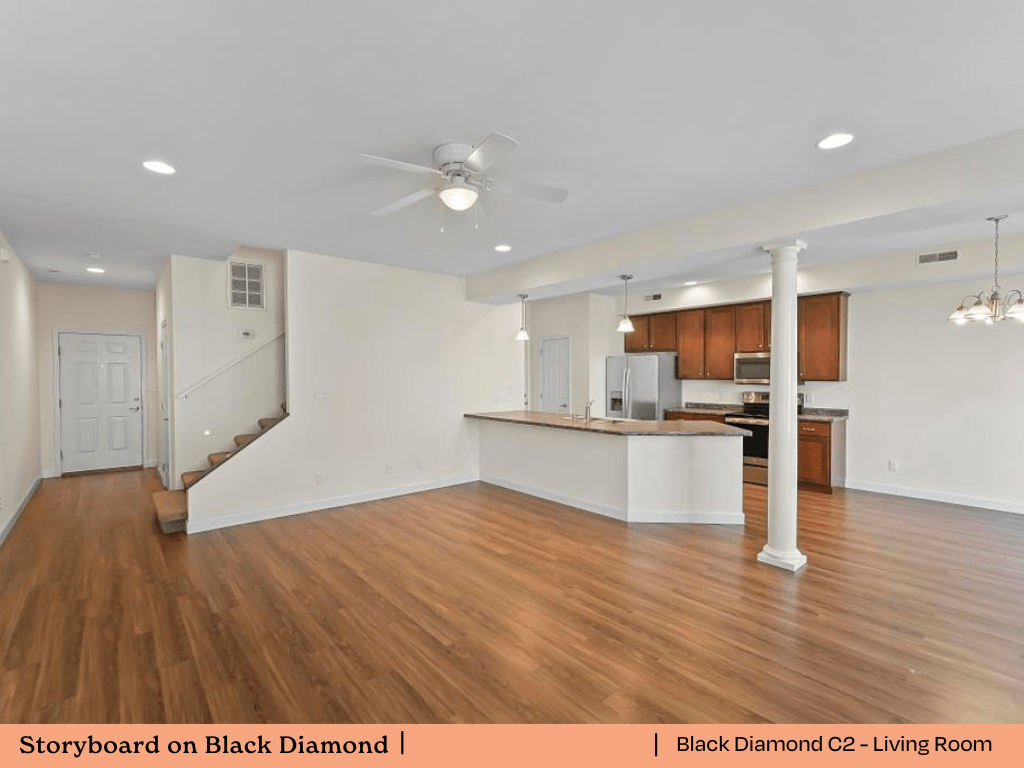 an empty living room with a kitchen and a ceiling fan