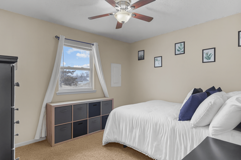 A bedroom with a bed, a window with curtains, and a ceiling fan.