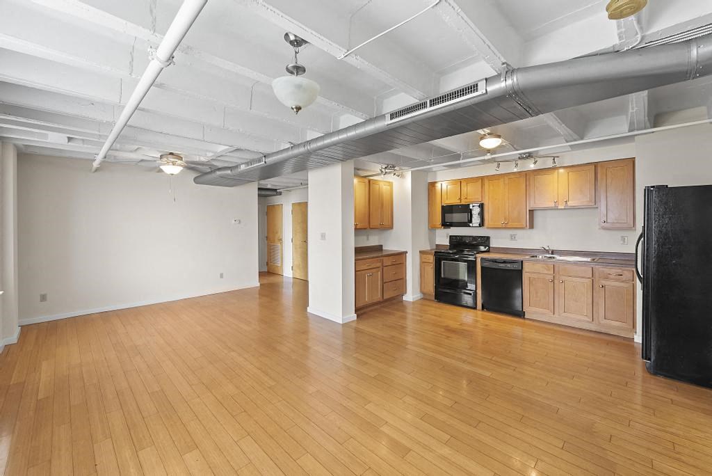 an empty room with a wood floor and a black refrigerator