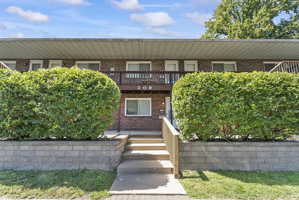 a brick building with a porch and two large bushes in front of it