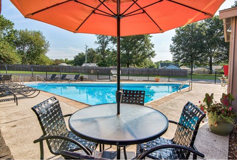 A table with chairs and an umbrella is set up by a pool.