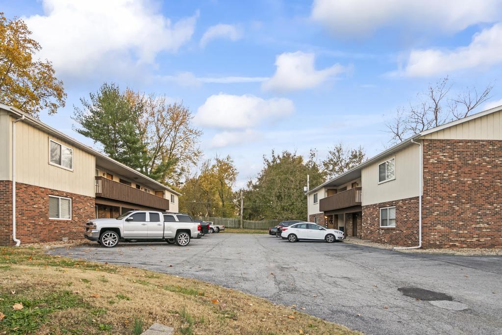 a parking lot between two apartment buildings with cars parked
