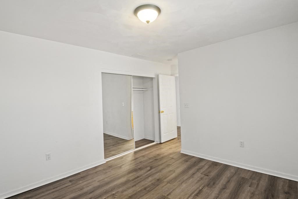 a bedroom with white walls and wood flooring and a closet