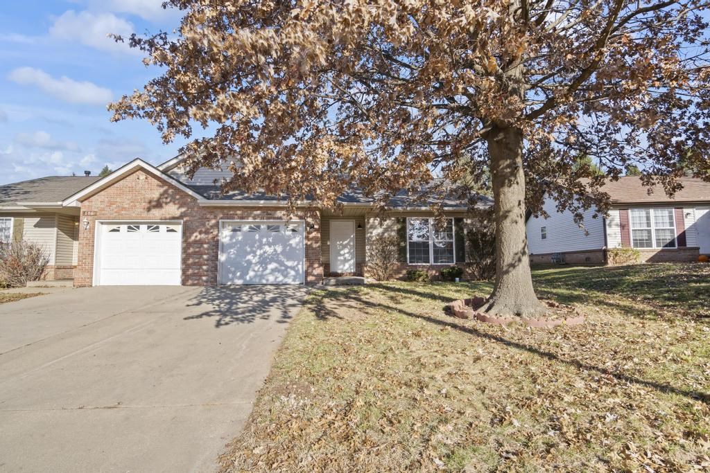 a house with a tree and a driveway in front of it