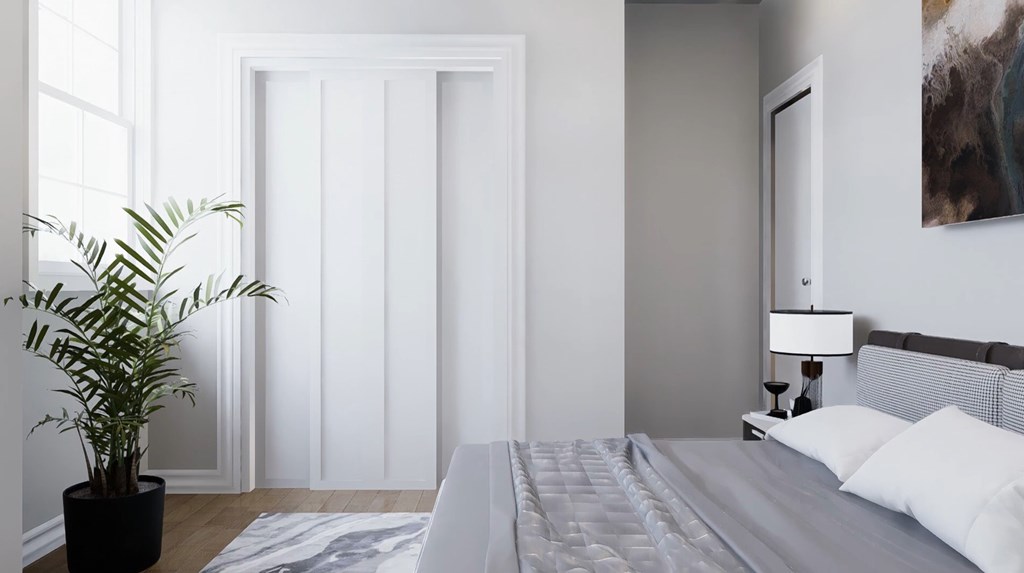 A bedroom with a bed, nightstand, lamp, and a plant.