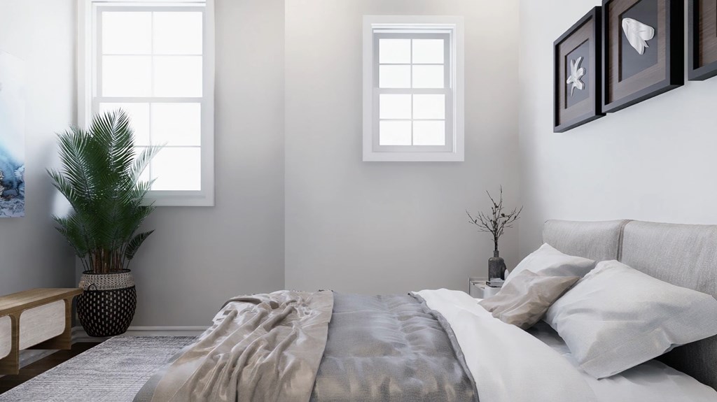 A bedroom with a bed, pillows, a plant, and pictures on the wall.