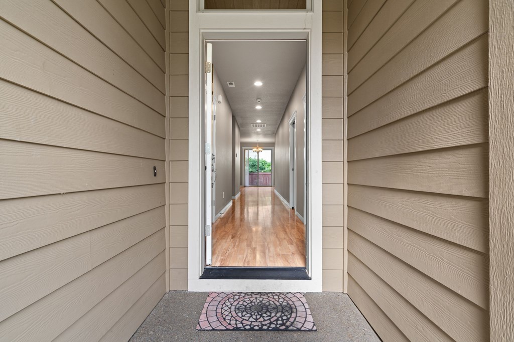 A hallway with a wooden floor and a rug in front of a glass door.