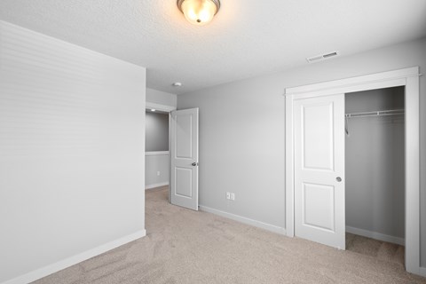 A white bedroom with a carpeted floor and a ceiling light.