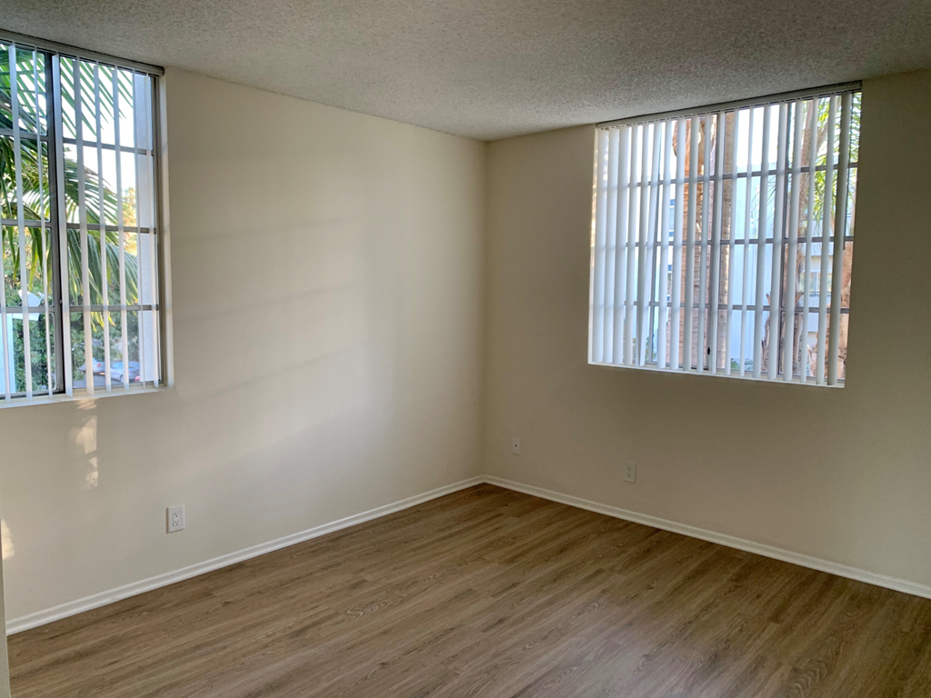 A room with wooden flooring and two windows.