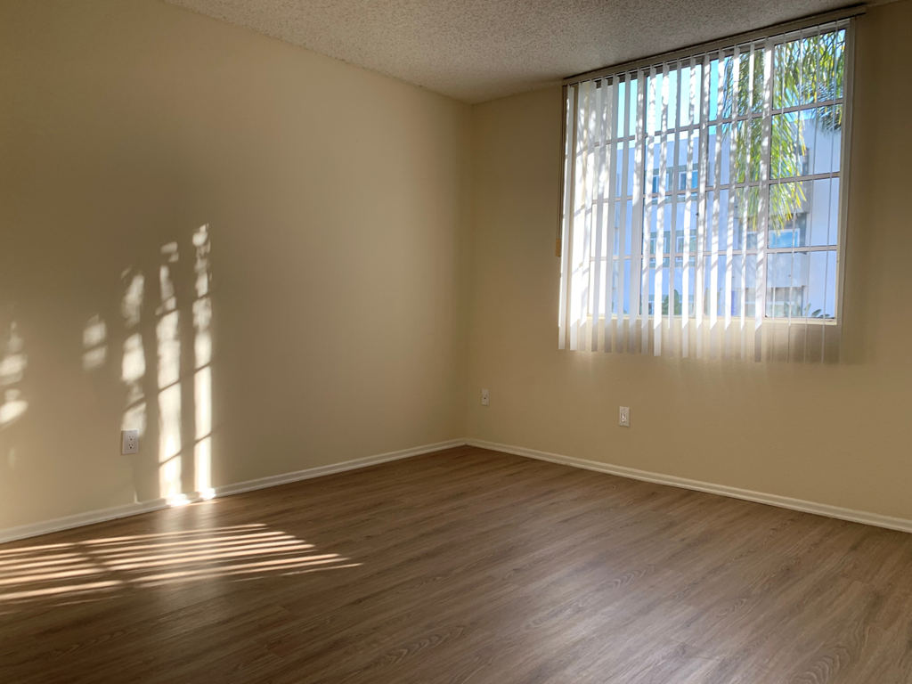 A room with wooden flooring and a window letting in sunlight.