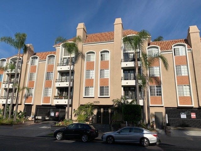 A large apartment building with a black car and a silver car parked in front.