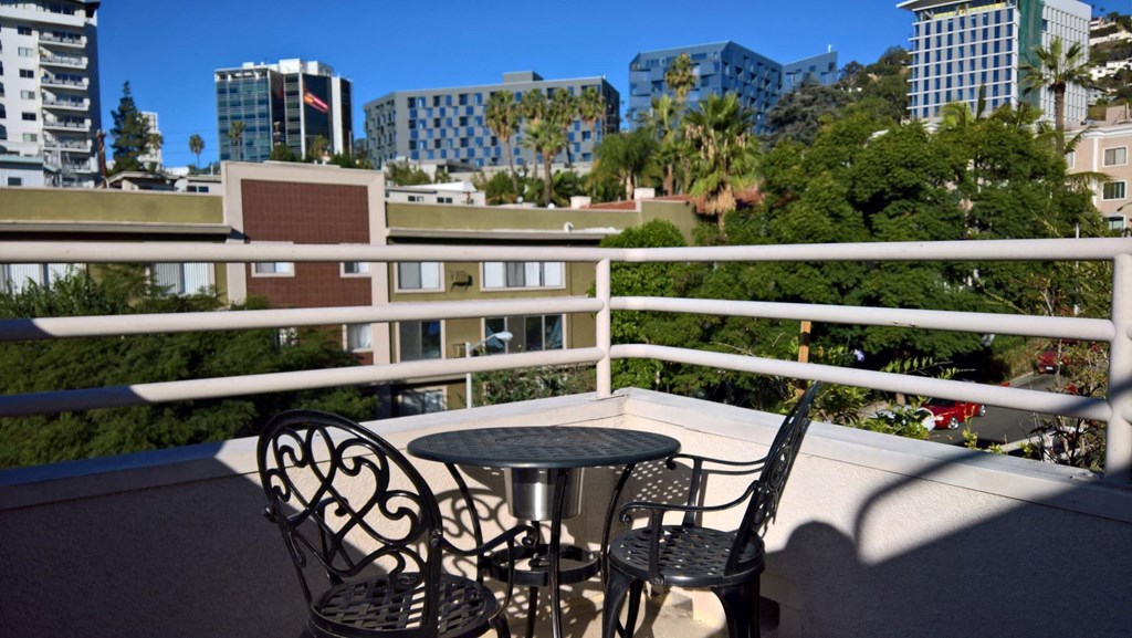 A balcony with a table and chairs overlooking a cityscape.