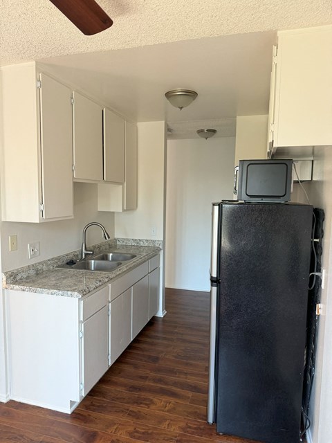 A black fridge in a kitchen with white cabinets.