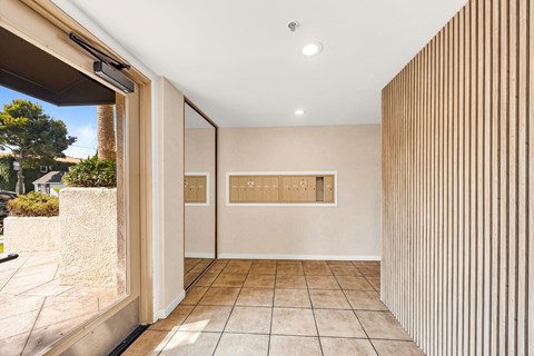 A hallway with a tan wall with mailboxes and a tan tile floor.