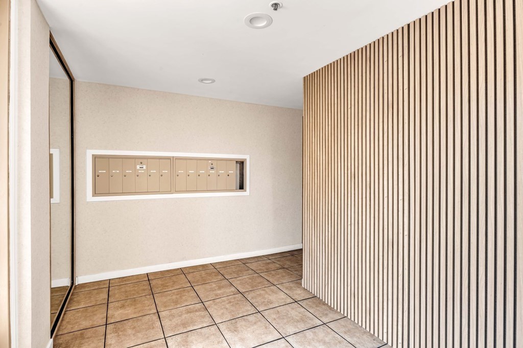A room with a wooden panel on the wall with mailboxes.