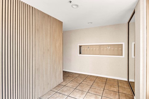 A hallway with a tan wall with mailboxes and a tan tile floor.