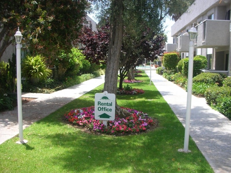 a rental office sign in front of a tree in the grass