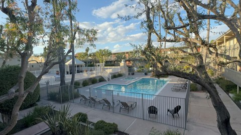 A pool surrounded by trees and chairs.