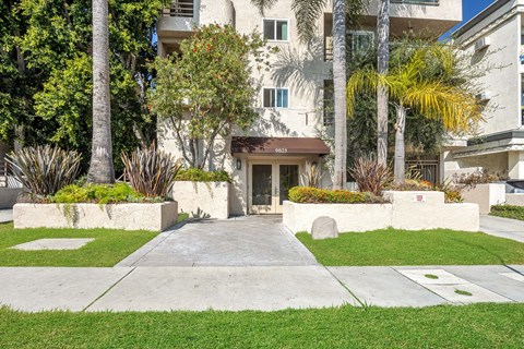 Image of 9025 Alcott Apartment building with a brown awning is surrounded by greenery.